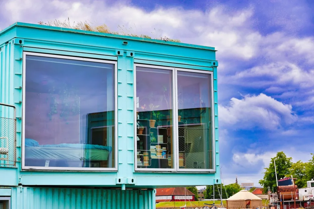 Durée de vie d'une maison container : façade turquoise de conteneurs aménagés avec de grandes fenêtres.